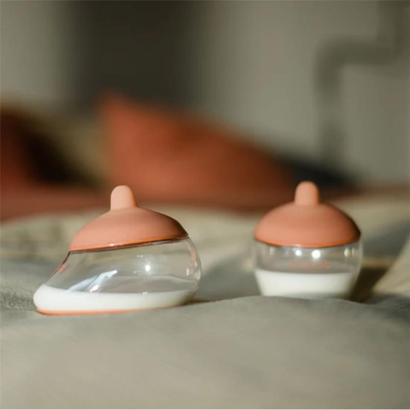 Emulait glass classic bottles with medium nipples, featuring pink tops and a smooth curved shape, on a soft surface.