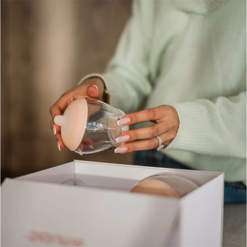 A woman holding a transparent bottle with a light-colored nipple, unpacking the Emulait Starter Kit.