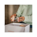 A person holding an Emulait starter kit nipple with color rich and shape 5, beside an open white box.
