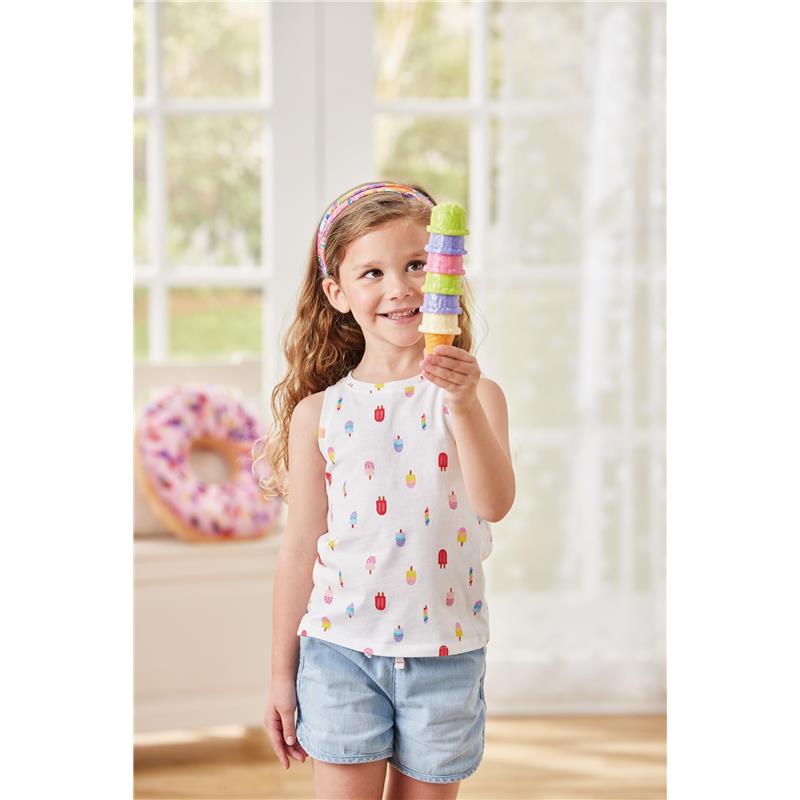 Young girl in a sleeveless patterned shirt holding a colorful ice cream cone with four scoops, smiling.