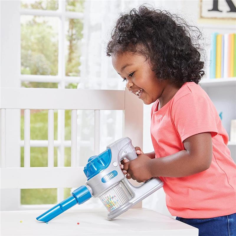 Child with curly hair happily using the Epoch Tidy Vacuum Duo toy on a table, cleaning up colorful beads.