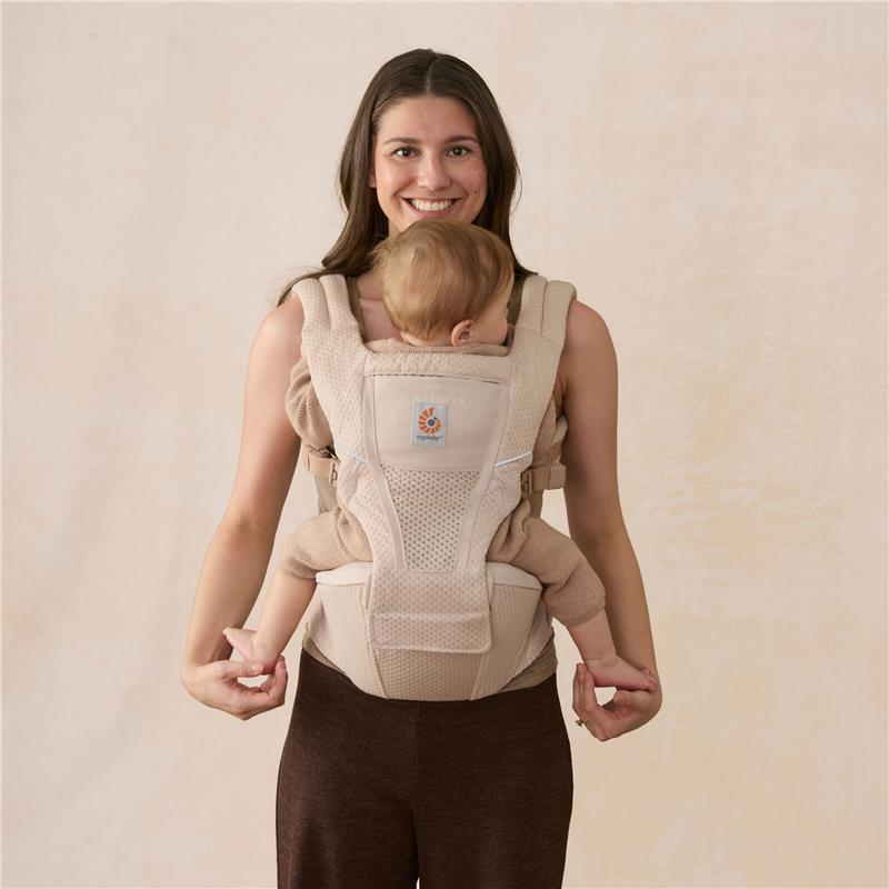 Ergobaby Alta Hip Seat Baby Carrier in natural beige, worn by a smiling woman holding a toddler securely.