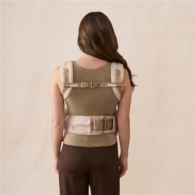 Ergobaby Alta Hip Seat Baby Carrier in natural beige, shown on a woman from the back, featuring padded straps and adjustable buckles.