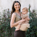 A woman holds a toddler in the Ergobaby Alta Hip Seat Baby Carrier, shown in natural beige color.