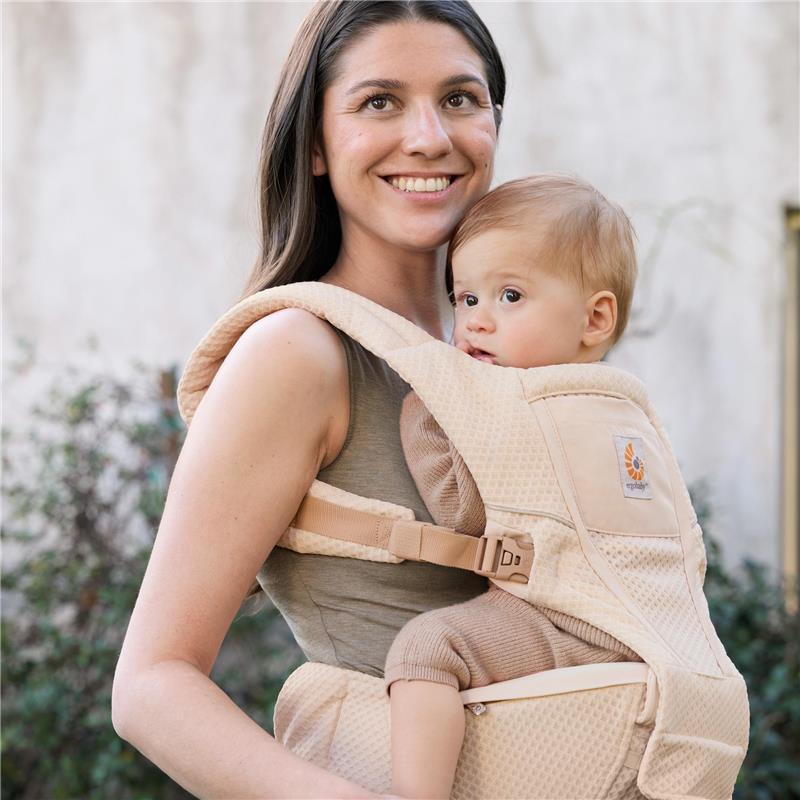 Ergobaby Alta Hip Seat Baby Carrier in natural beige, worn by a smiling woman holding a baby, showcasing comfort and support.