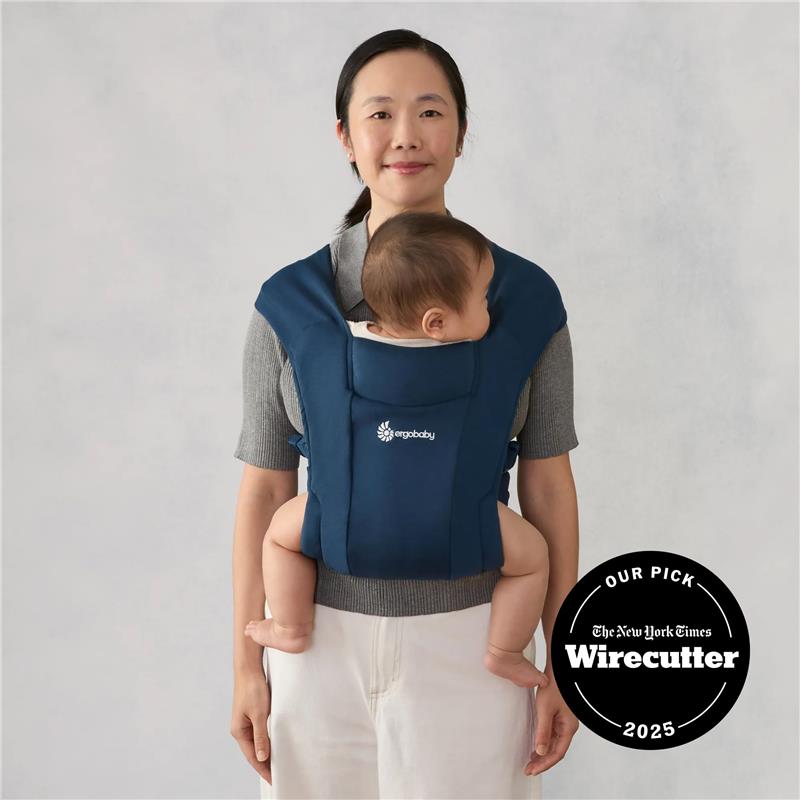 Ergobaby Embrace newborn baby carrier in navy, worn by a woman holding a baby, features the brand logo prominently.
