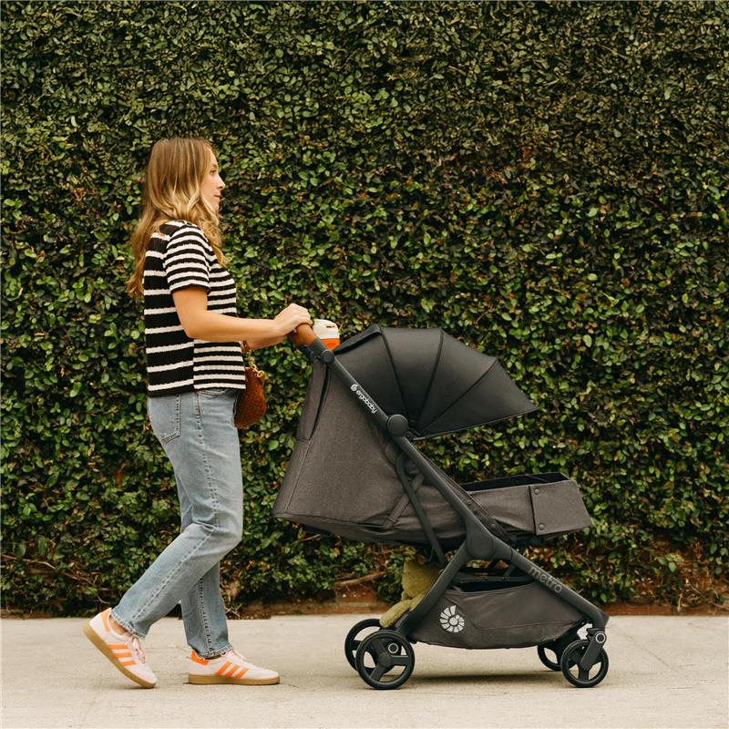 A woman walks alongside a camel-colored Ergobaby Metro 3 Deluxe Baby Stroller, featuring a canopy and storage basket.