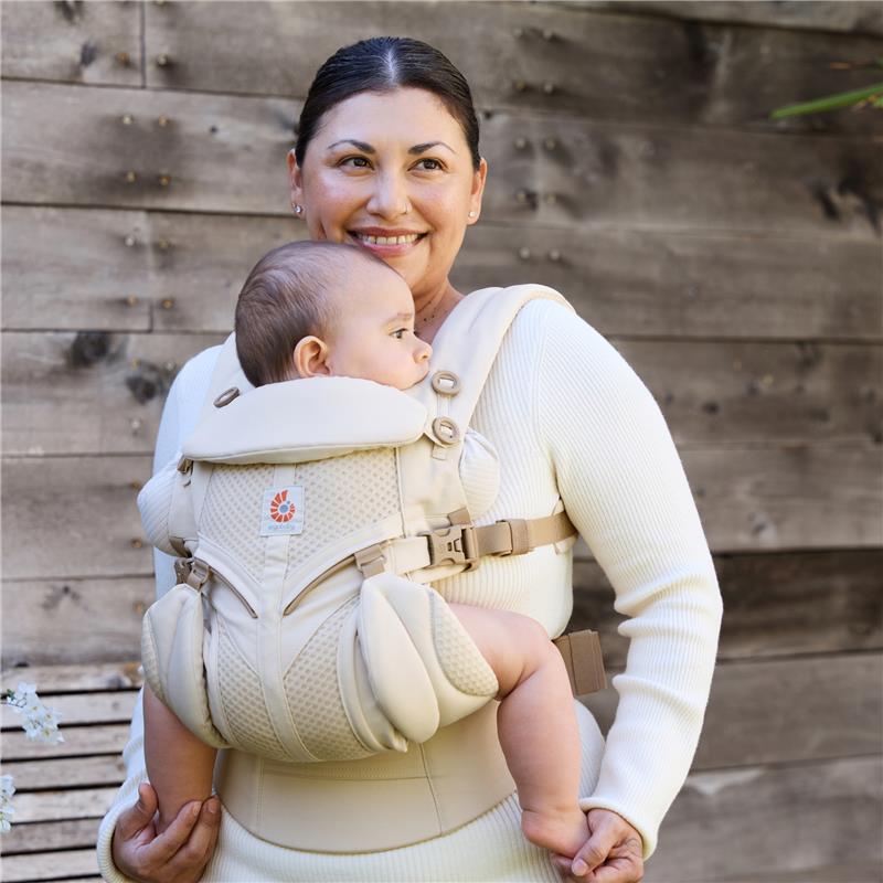 Ergobaby Omni Classic Baby Carrier in Natural Beige, worn by a smiling woman with a baby facing outward.