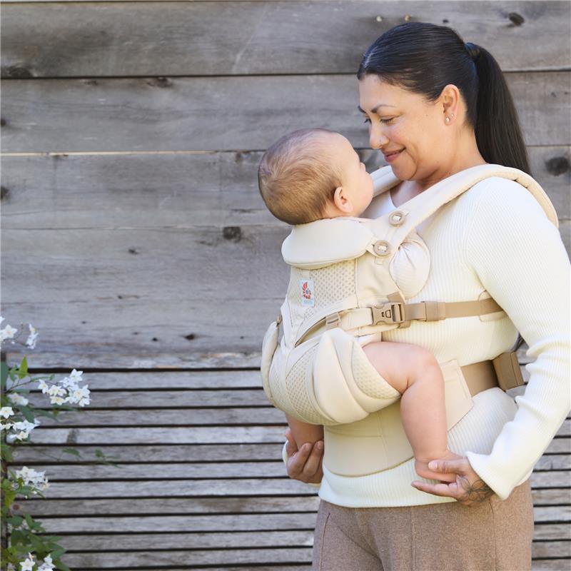 Ergobaby Omni Classic Baby Carrier in Natural Beige, worn by a woman holding her baby, both smiling at each other.