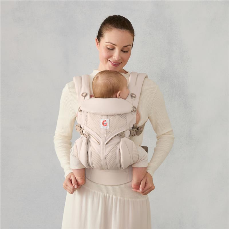 Ergobaby Omni Classic Baby Carrier in natural beige, worn by a smiling woman, securely holding a visibly content baby.
