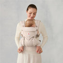 Ergobaby Omni Classic Baby Carrier in natural beige, worn by a smiling woman, securely holding a visibly content baby.
