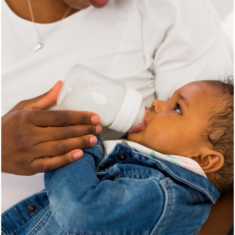 Baby drinking from an Evenflo Feeding 9 oz Balance + Wide Bottle, held by a caregiver, in a cozy setting.