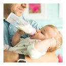 A baby drinking from an Evenflo Feeding classic clear plastic bottle while being held by an adult.