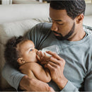 Father holding a baby feeding with an Evenflo 4 oz glass bottle, both relaxed on a couch.