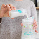 A person pours milk from an Evenflo feeding bottle into a storage pouch, featuring floral designs and motivational text.