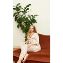 Maternity and nursing pajama pant set in mocha stripe on a pregnant woman seated on a brown couch with a leafy plant.