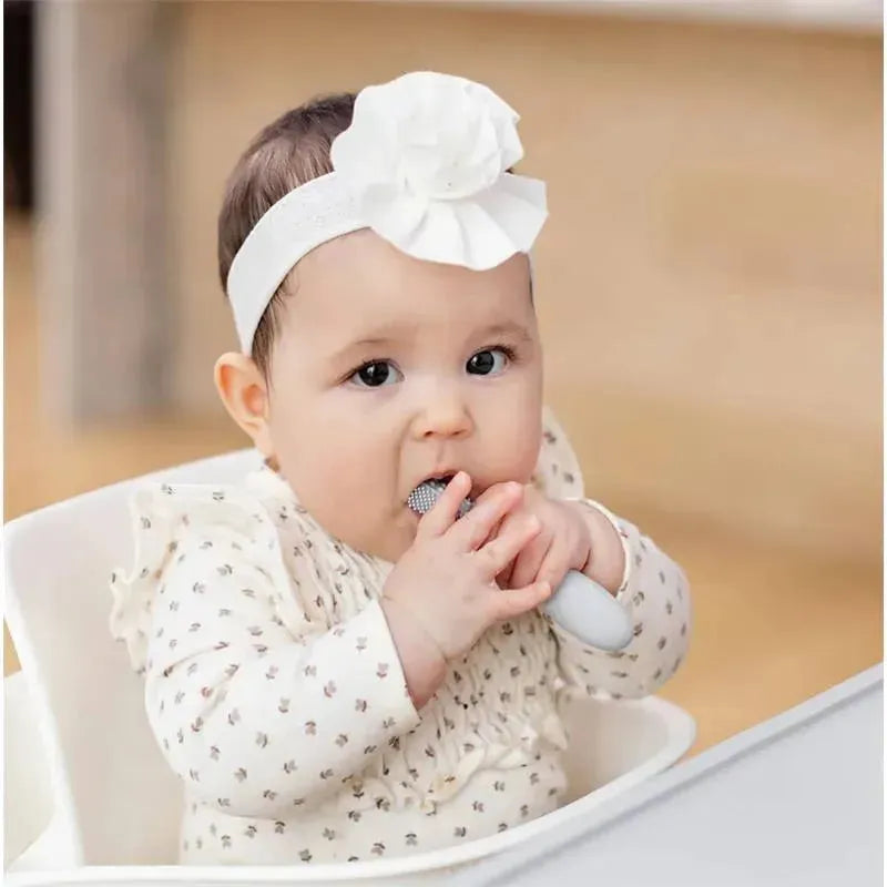 Baby using the Ezpz Baby-Led™ Toothbrush, a gray toothbrush with a textured head, while sitting in a high chair.