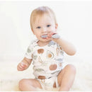 Toddler using a gray Ezpz Baby-Led toothbrush while sitting on a soft surface, wearing a patterned onesie.