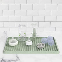 A sage-colored drying rack features various baby bottles, pacifiers, and utensils, designed for drying clean items.