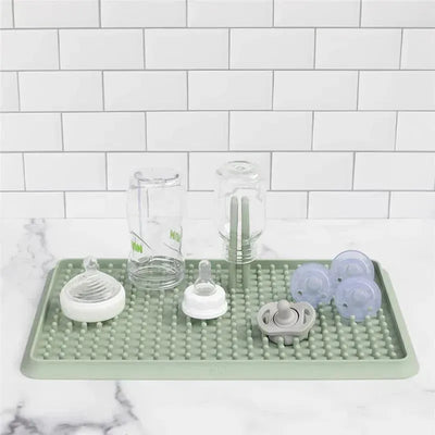 A sage-colored drying rack features various baby bottles, pacifiers, and utensils, designed for drying clean items.