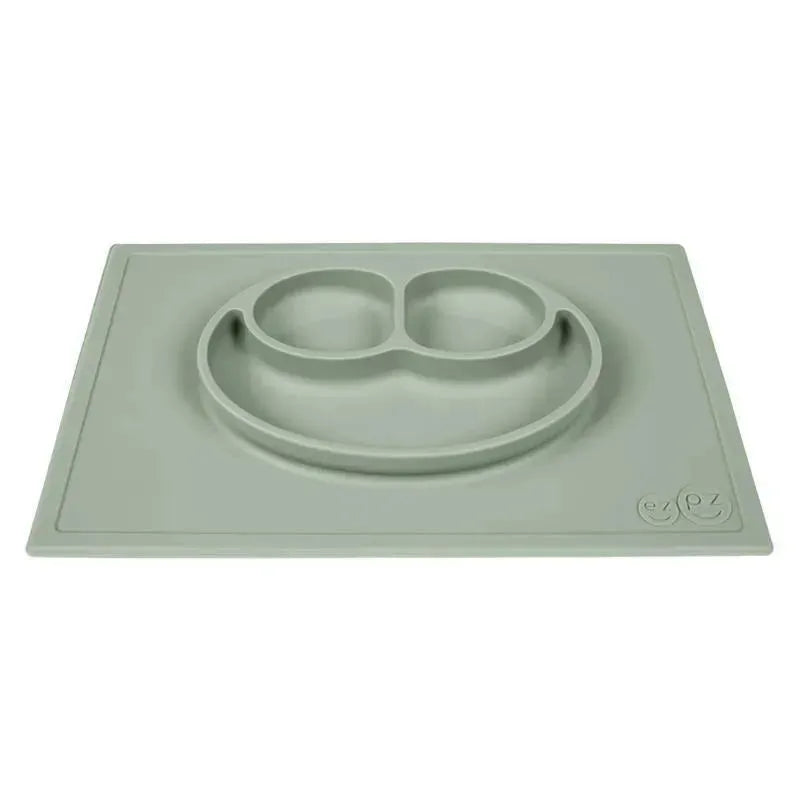 Sage green silicone Happy Mat by Ezpz featuring a smiling face design with two divided sections for food.