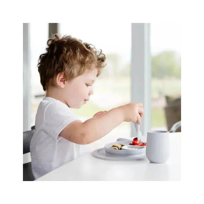 Child using the Ezpz Mini Feeding Set in pewter color, engaged in self-feeding with a spoon, featuring fruit and pancakes on a plate.