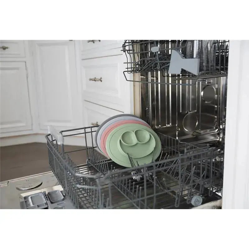 Ezpz Mini Mat in blush, placed in a dishwasher alongside additional silicone mats in various colors.