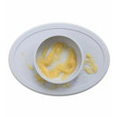 Ezpz Tiny Bowl in pewter color, featuring a curved edge, with a portion of yellow food inside and some spilled around.