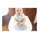 A toddler sitting in a high chair with a gray Ezpz Tiny Bowl containing small food items and a few pieces of asparagus.