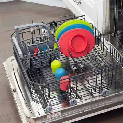 Colorful silicone Ezpz Tiny Cups and plates arranged in a dishwasher alongside utensils in a cutlery basket.