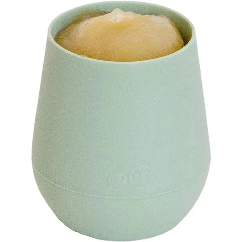 Sage-colored Ezpz Tiny Cup filled with a creamy substance, designed for young children to drink from easily.