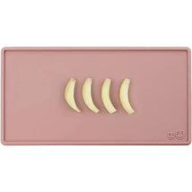 Tiny placemat in blush color featuring four banana slices arranged on it.