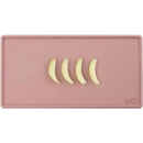Tiny placemat in blush color featuring four banana slices arranged on it.