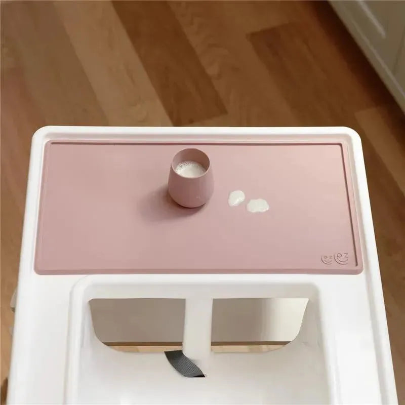 Tiny placemat in blush color features a small cup with liquid and two white droplets on a clean surface.