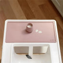 Tiny placemat in blush color features a small cup with liquid and two white droplets on a clean surface.