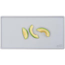 Tiny pewter-colored placemat with three avocado slices arranged on it.