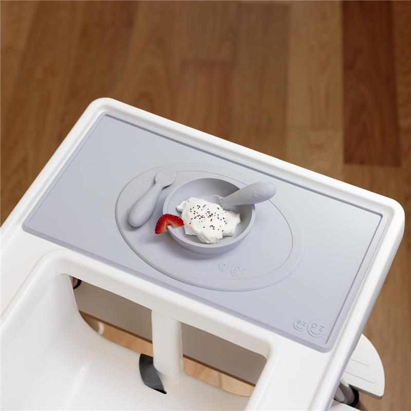 Ezpz Tiny Placemat in pewter color with a small bowl containing whipped cream and a strawberry slice, placed on a high chair tray.
