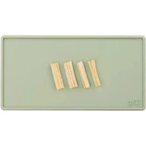 Sage-colored Ezpz Tiny Placemat with four strips of food displayed on it.
