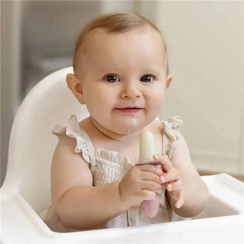 Baby seated in a high chair holding a pink blush popsicle mold with a light-colored popsicle inside.