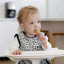 Toddler sitting in a high chair enjoying a popsicle from the Ezpz Tiny Popsicle Mold Set, wearing a spotted bib.