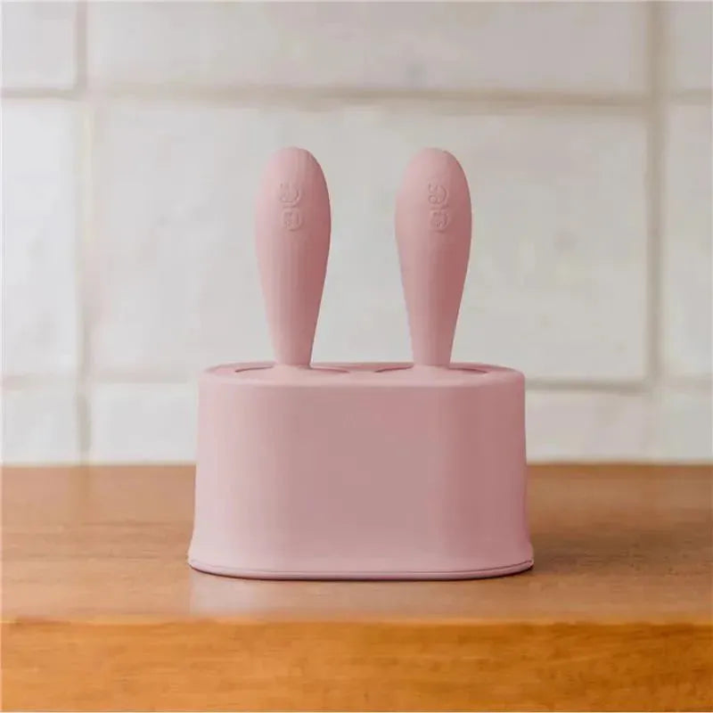 Tiny pink silicone popsicle mold set with two wands, designed for making frozen treats, placed on a wooden surface.