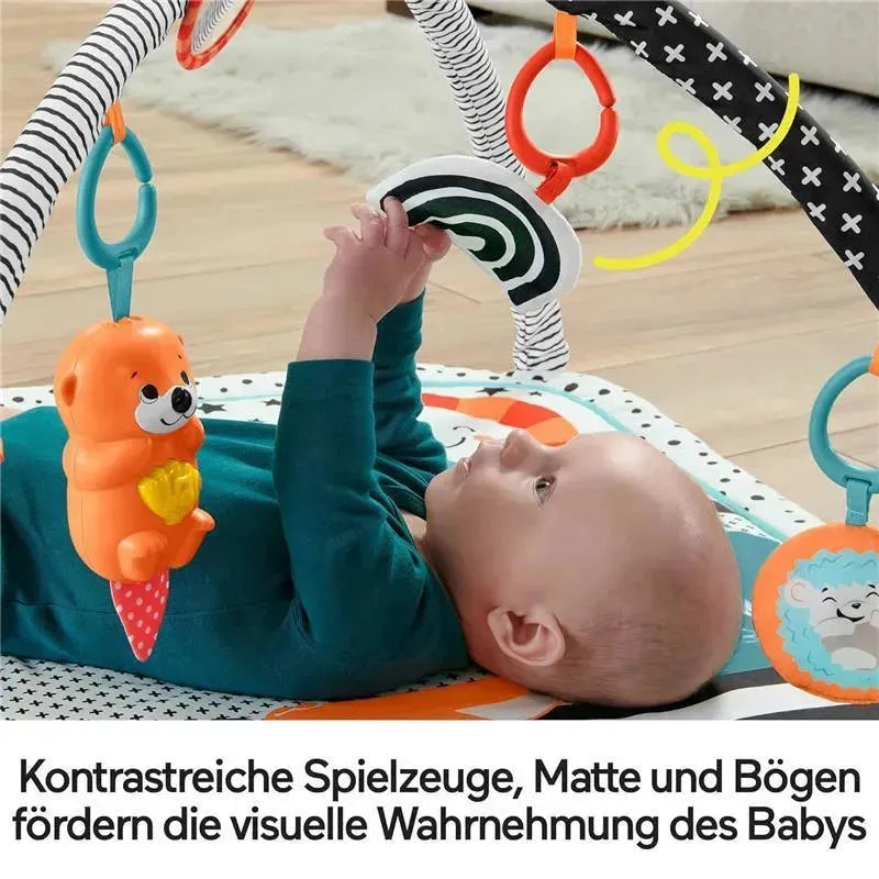 Baby lying on a colorful Fisher Price play mat, reaching for a hanging toy and a black-and-white spiraled object.