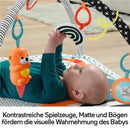 Baby lying on a colorful Fisher Price play mat, reaching for a hanging toy and a black-and-white spiraled object.