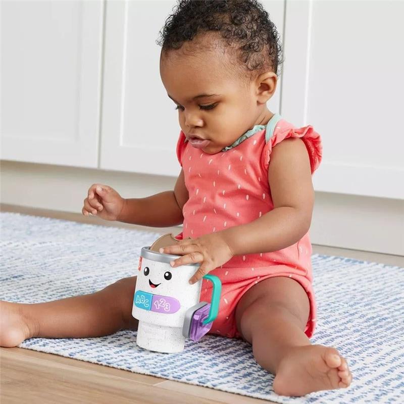 Toddler in a pink outfit plays with a Fisher Price Laugh & Learn Coffee Mug toy featuring lights and sounds.