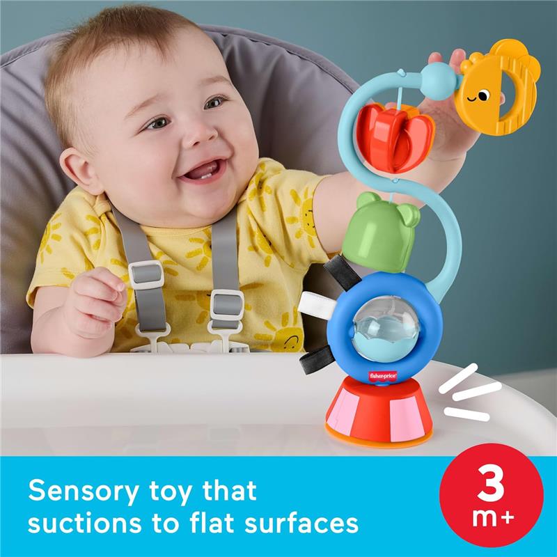 Baby in a high chair smiles while playing with the Fisher-Price sensory toy featuring colorful shapes and suction base.