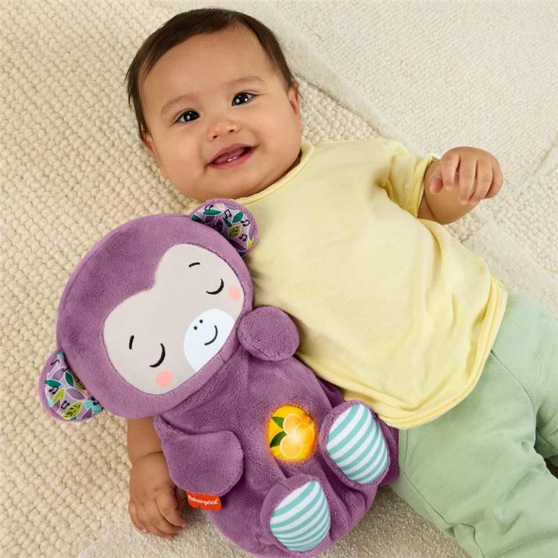 Baby smiling while lying on a blanket, holding a purple plush monkey toy with a smiley face and striped feet.
