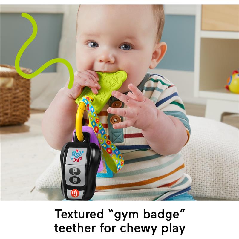 A baby is playing with the Fisher Price Laugh & Learn Activity Keys, featuring a textured green teether and colorful straps.