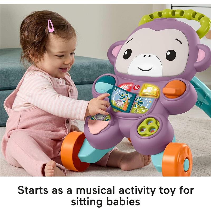 A smiling baby girl in pink overalls interacts with a colorful Fisher-Price purple monkey baby walker, pressing buttons that light up and play music.