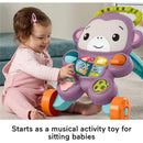 A smiling baby girl in pink overalls interacts with a colorful Fisher-Price purple monkey baby walker, pressing buttons that light up and play music.