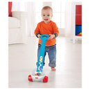 Child pushing a Fisher Price Corn Popper toy with colorful balls inside, wearing an orange shirt and denim pants.